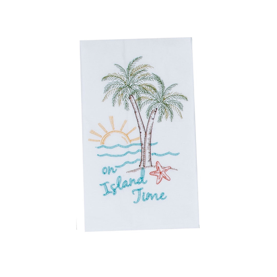 white towel embroidered with scenes of palms trees, sunset over the ocean, a starfish and “on island time”
