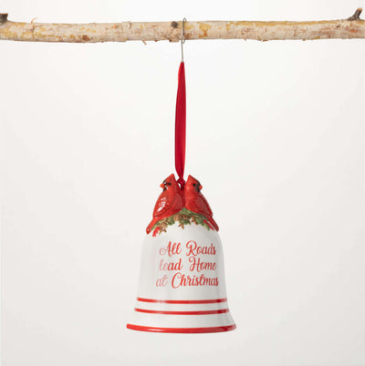Red and white bell ornament topped with red cardinals reads “All Roads Lead Home at Christmas”
