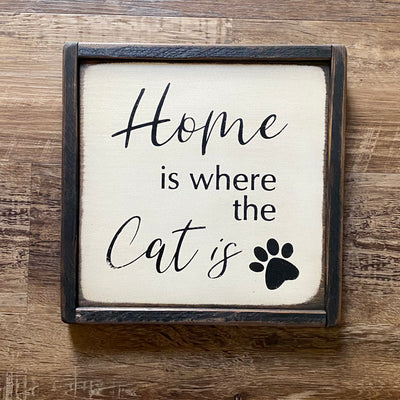 10x10 framed wood sign reads home is where the cat is. White background with black lettering.
