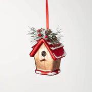 Glass birdhouse ornament features a bright red roof, a dusting of snow, and of greens and berries on top with a red ribbon for haning