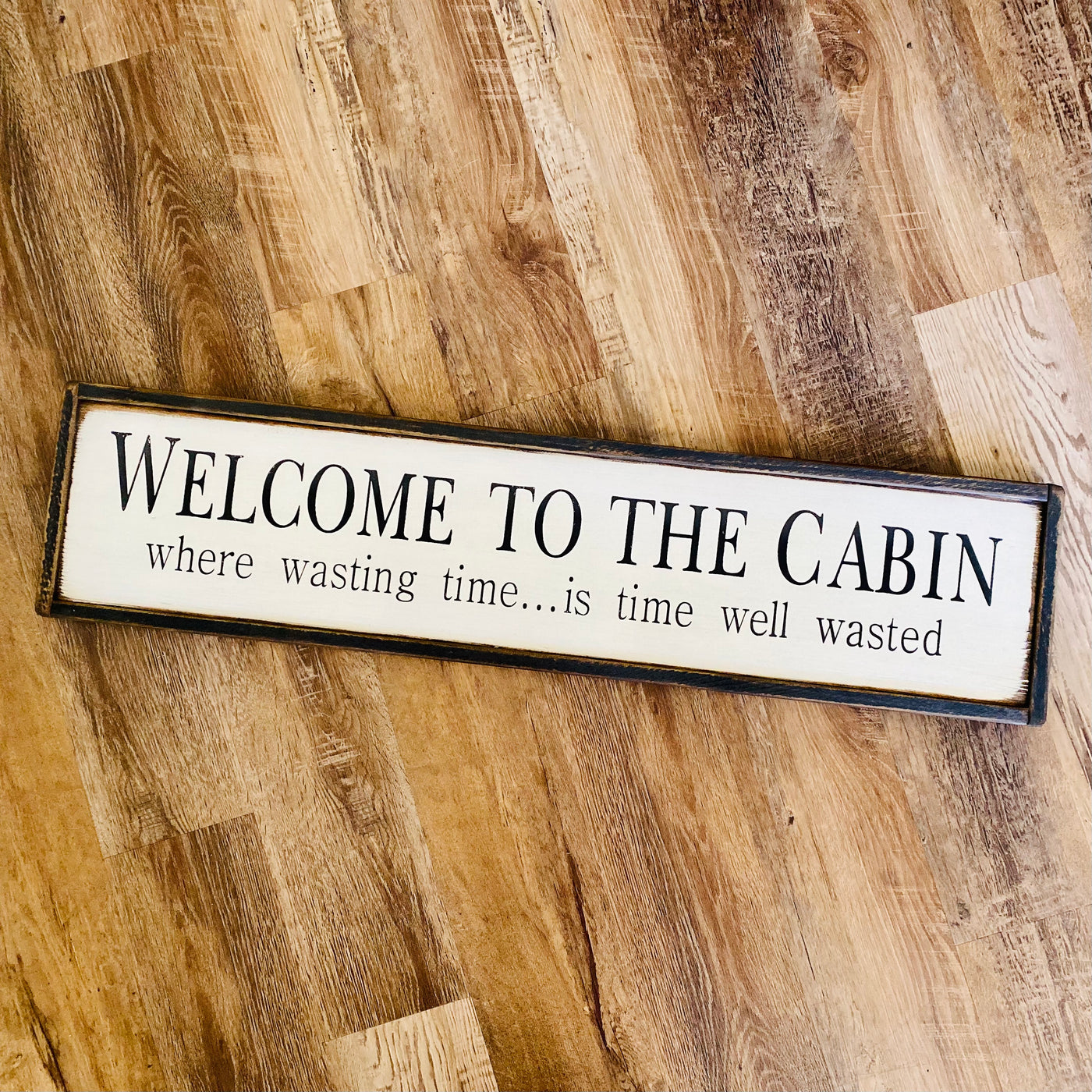 Handmade wood sign reads Welcome To The Cabin where wasting time….is time well wasted