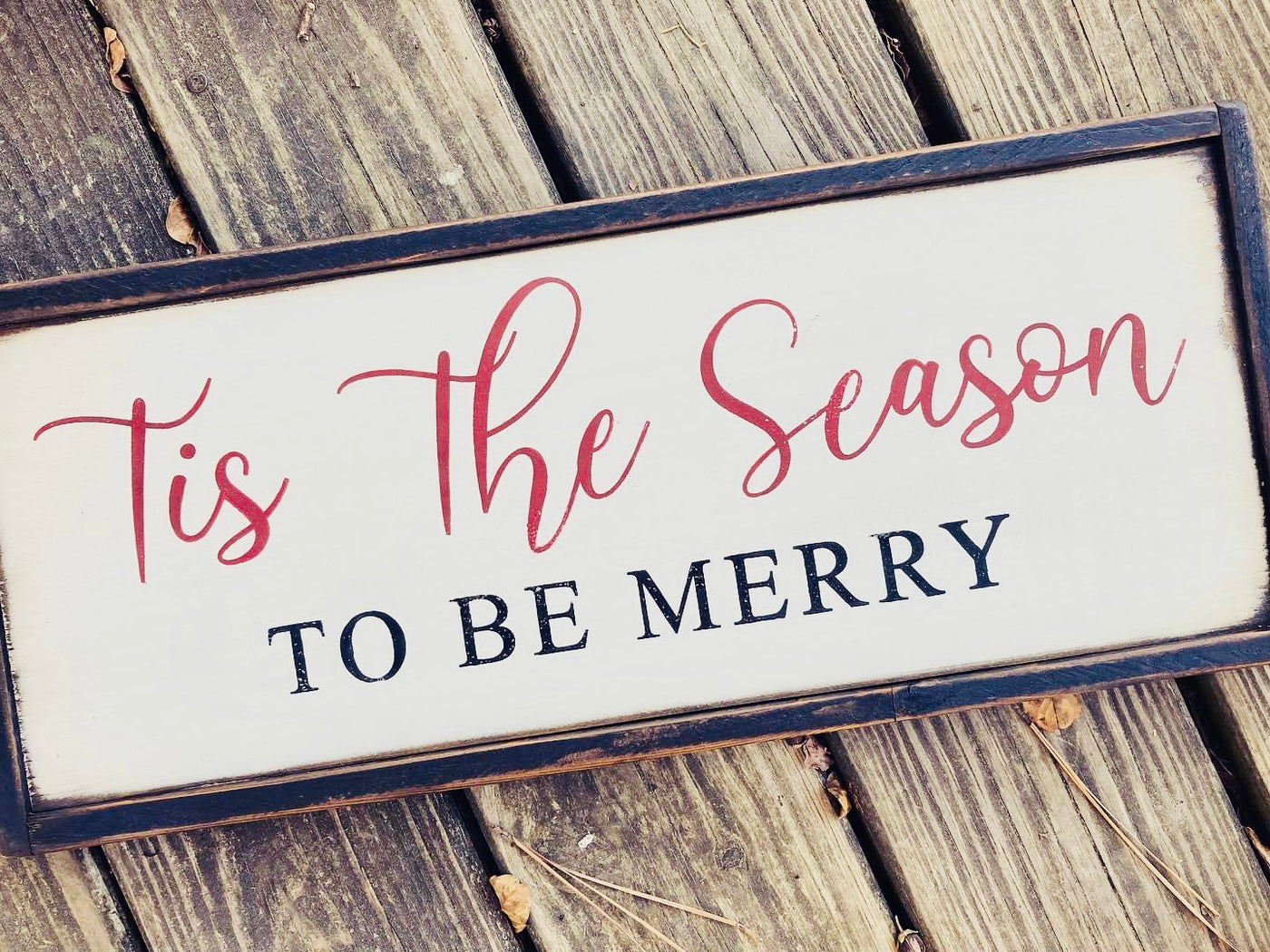 Handmade wooden holiday sign reads this the season to be merry. White background with red and black lettering.
