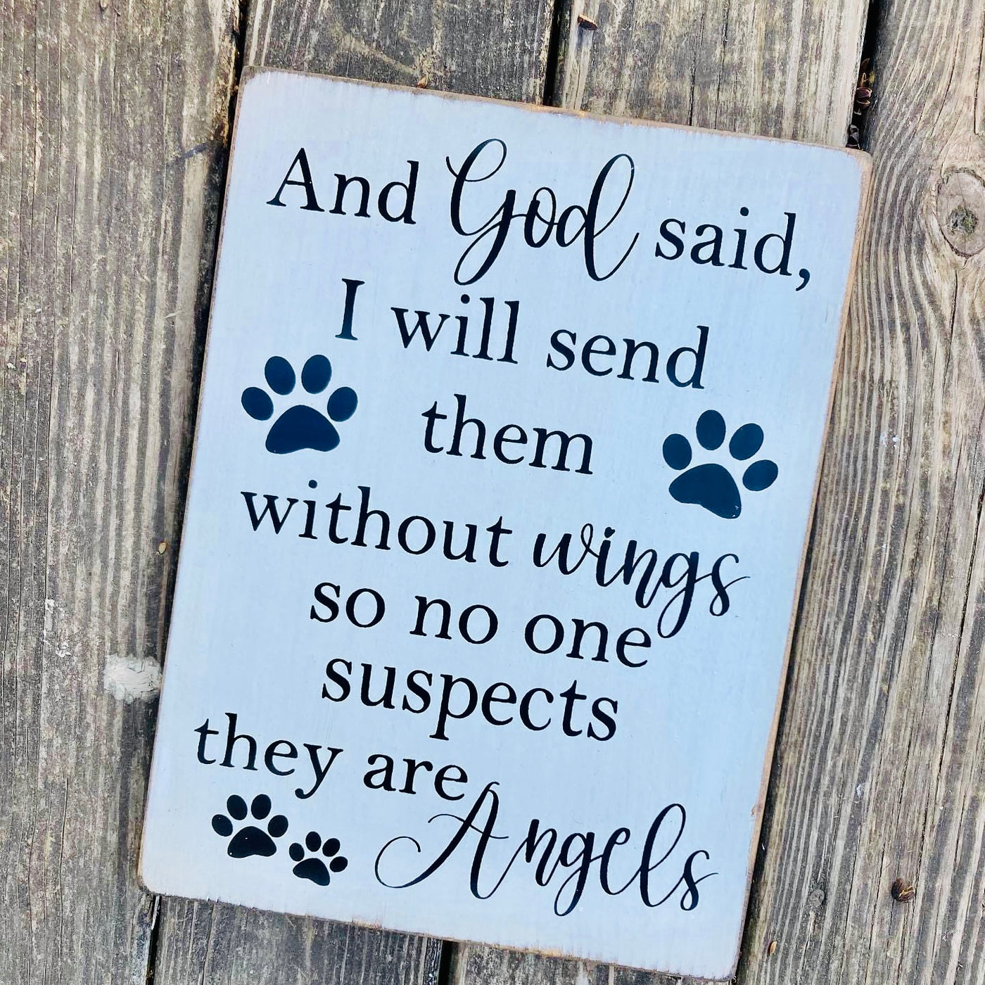 Handmade wood sign reads And God said, I will send them without wings so no one suspects they are Angels. White sign with black lettering and paw print accents.