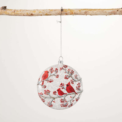 Round glass disc ornament featuring a painted snowy cardinal scene