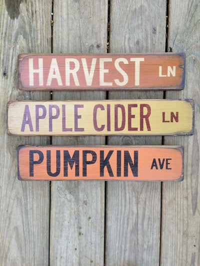 Three wood signs read Pumpkin Ave, Harvest Ln, and Apple Cider Lane