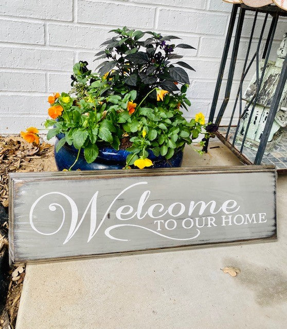 Handmade wood sign with decorative edge reads Welcome to Our Home